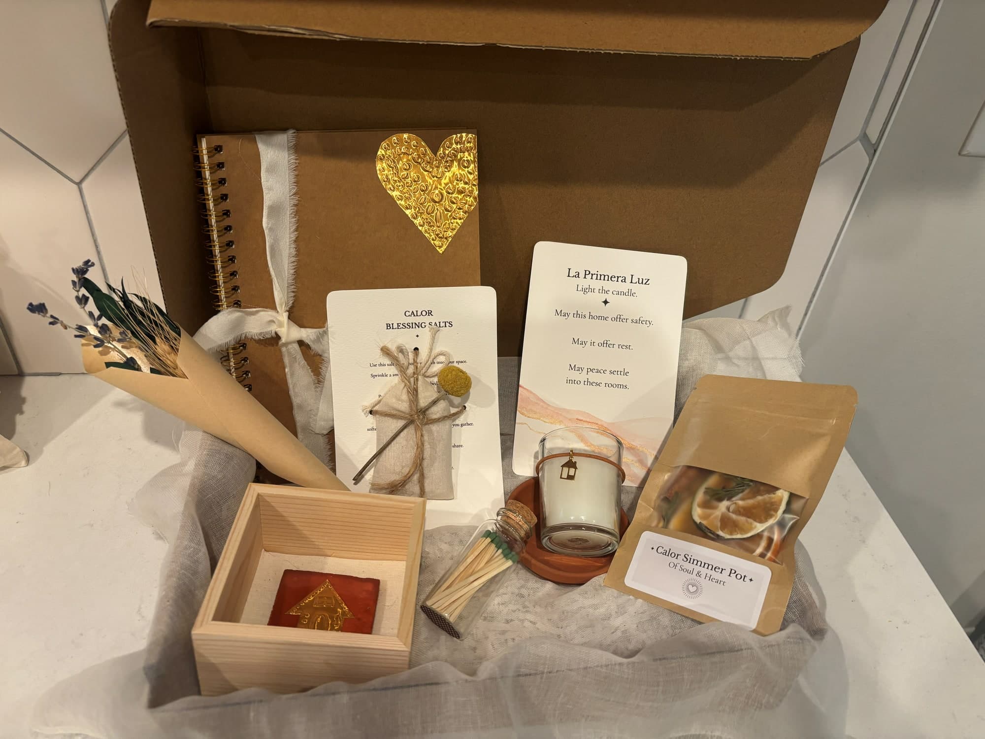 A Casa box seen from the side, with a framed terracotta house tile, blessing cards, a small candle and a Calor simmer pot nested in gauze