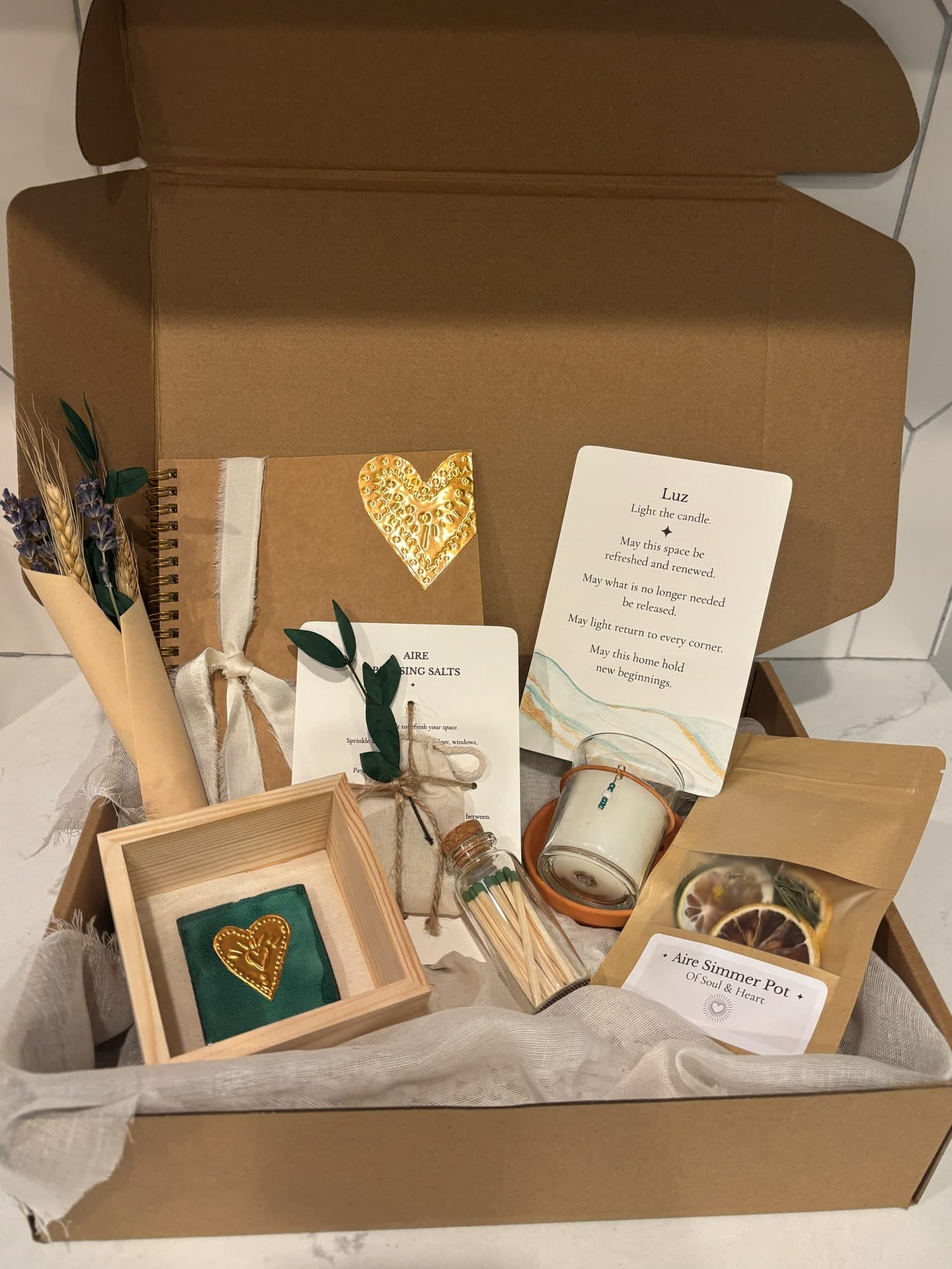 An open Casa gift box with a gold-heart journal, a blessing card, Aire blessing salts, a framed teal tile, matches, a small candle and a simmer pot - a handmade housewarming gift