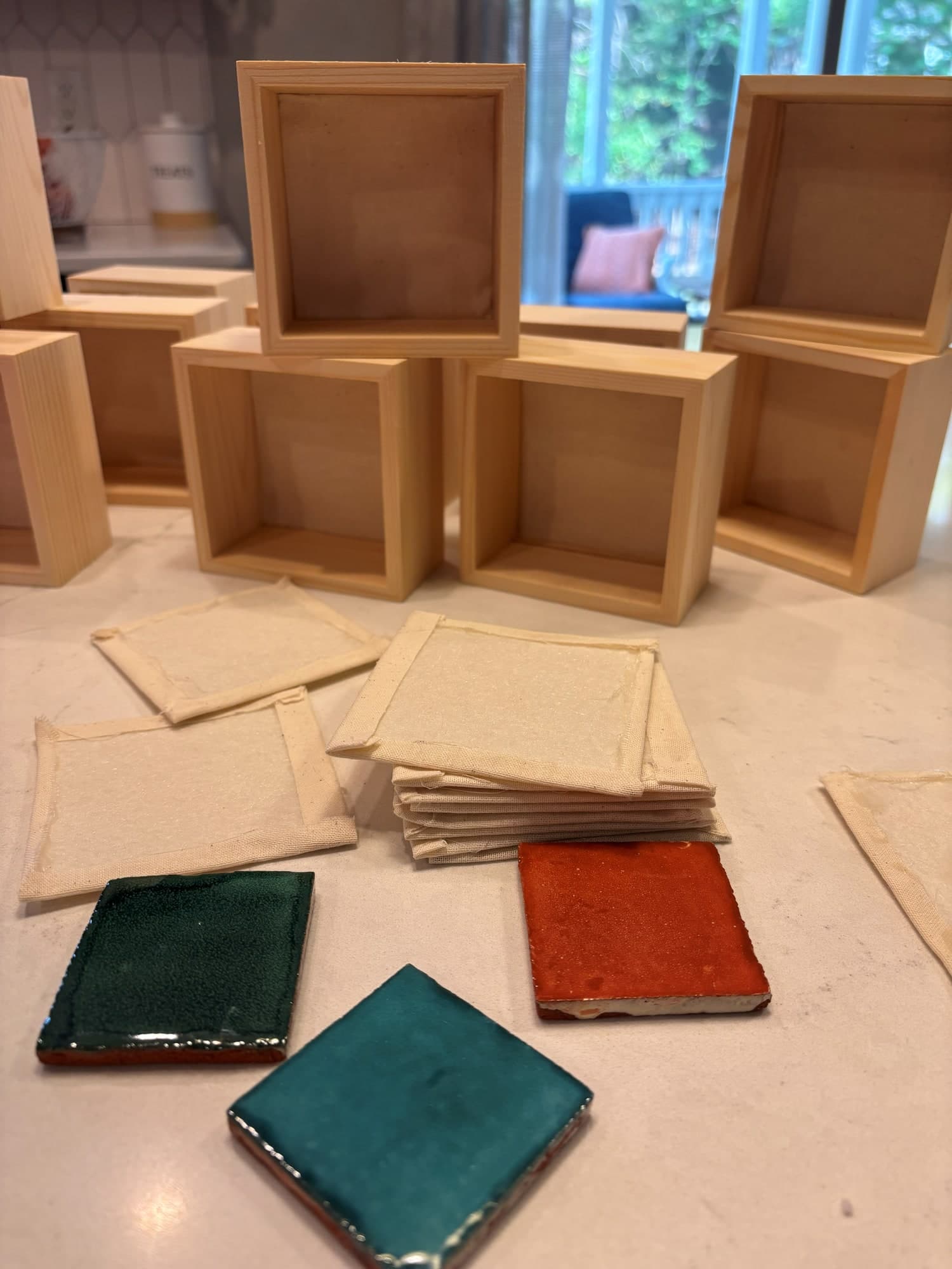 Glazed teal and terracotta tiles, linen squares and small wooden frames laid out on a table